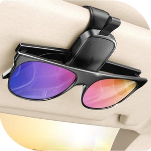 Puede incluir: Un soporte negro para gafas de sol para visera de coche con un par de gafas de sol. Las gafas de sol tienen una montura negra y lentes con un degradado de colores, incluyendo morado, rosa y naranja.