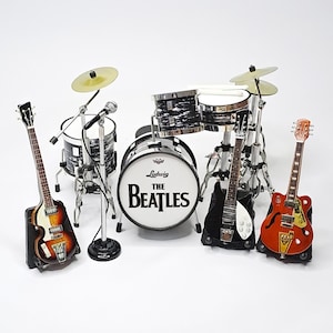 Może przedstawiać: Miniaturowy zestaw perkusyjny z talerzami, mikrofonem i trzema gitarami. Bęben basowy z logo "The Beatles". Gitary w różnych kolorach, w tym brązowym, czarnym i pomarańczowym. Zestaw perkusyjny jest czarny i srebrny.