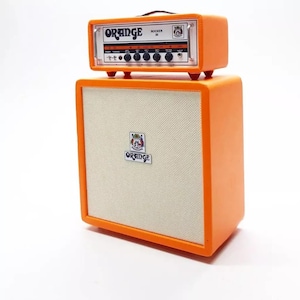 Könnte beinhalten: Ein orangefarbener Gitarrenverstärker und Lautsprecherbox-Set. Der Verstärker mit der Aufschrift "Orange Rocker 30" steht auf der Lautsprecherbox. Beide Teile sind orange mit weißen und silbernen Akzenten. Die Lautsprecherbox hat eine cremefarbene Lautsprecherabdeckung.