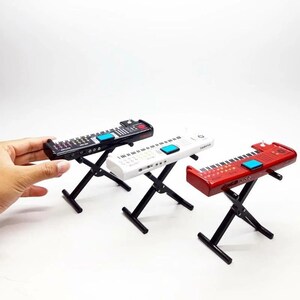 May include: Three miniature toy keyboards in black, white, and red, each with a blue accent button and a black stand. The keyboards have a piano key design and are set against a white background.