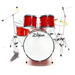 May include: A miniature red drum kit with silver stands and cymbals. The bass drum has the "Zildjian" logo in black. The set includes a bass drum, snare drum, two tom-toms, and cymbals, all on adjustable stands.