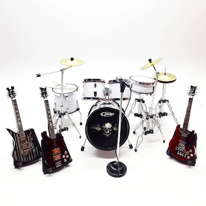 May include: Miniature rock band set featuring a white drum kit, cymbals, a microphone, and three electric guitars. The drum set has a black bass drum with a skull graphic. The guitars are black and red.