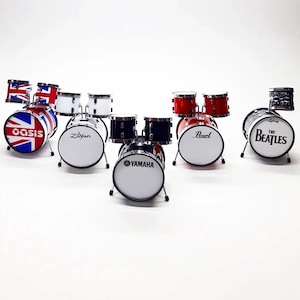 Könnte beinhalten: Miniatur-Schlagzeug-Sets in verschiedenen Farben und Designs, darunter rot, schwarz, weiß und ein Schlagzeug mit der Flagge des Vereinigten Königreichs. Einige Trommeln tragen die Namen "Oasis", "Zildjian", "Pearl", "Yamaha" und "The Beatles".