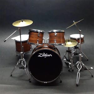 Könnte beinhalten: Miniatur-Schlagzeug mit Zildjian-Logo auf der Bassdrum. Das Set enthält eine Bassdrum, Snare, zwei Tom-Toms, eine Standtom und Becken. Die Trommeln sind braun mit silberner Hardware und die Becken sind goldfarben.