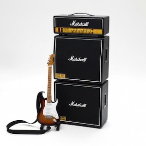 Könnte beinhalten: Miniatur-Marshall-Gitarrenverstärker-Stack mit einer braunen und weißen E-Gitarre. Der Verstärker-Stack ist schwarz mit dem Marshall-Logo und -Text. Die Gitarre hat einen schwarzen Gurt.
