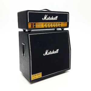 Könnte beinhalten: Ein schwarzer Marshall JCM 800 Lead Series Verstärker-Stack. Der Verstärkerkopf befindet sich oben auf der Lautsprecherbox. Der Kopf hat goldene und gelbe Akzente mit dem Marshall-Logo. Die Lautsprecherbox hat das Marshall-Logo und einen weißen Rand.