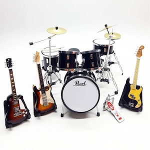 May include: A miniature black drum kit with cymbals, a bass drum with the word "Pearl", and three guitars. One guitar is brown, one is brown and white, and one is black and yellow. A red and white bass drum pedal is in front.