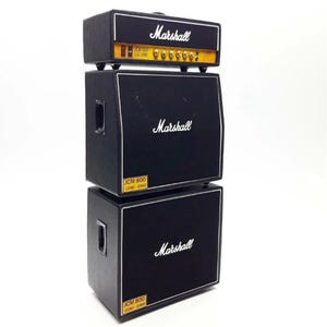 Könnte beinhalten: Ein Miniatur-Marshall-Verstärker-Stack in Schwarz. Das obere Gerät hat ein goldenes Bedienfeld und das Marshall-Logo. Die mittleren und unteren Einheiten sind schwarze Lautsprecherboxen mit dem Marshall-Logo und JCM 800 Lead 1960-Etiketten.