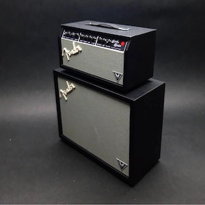 Könnte beinhalten: Zweiteiliges schwarzes Gitarrenverstärker-Set. Der obere Verstärker hat einen Griff und Bedienknöpfe. Beide Verstärker haben eine silberne Lautsprecherabdeckung mit dem Fender-Logo und einem V-förmigen Emblem.