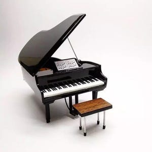 May include: A miniature black grand piano with a matching bench. The piano has white and black keys, a music stand with sheet music, and a glossy finish. The bench has a wooden seat and silver legs.
