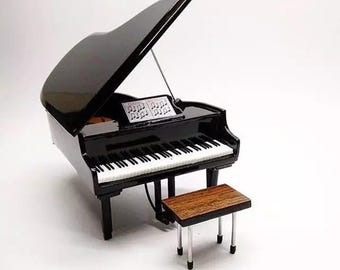 May include: A miniature black grand piano with a matching bench. The piano has white and black keys, a music stand with sheet music, and a glossy finish. The bench has a wooden seat and silver legs.