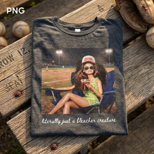 Puede incluir: Camiseta gris oscuro con un gráfico de una persona en un estadio de béisbol, con gafas de sol y una gorra que dice "Raising Ballers". El texto "literally just a bleacher creature" está impreso en la parte inferior del gráfico.