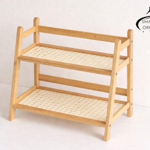 Könnte beinhalten: Ein zweistufiges Bambusregal mit gewebten Rattanböden. Der hellbraune Holzrahmen hat eine rechteckige Form mit einem Logo in der oberen rechten Ecke mit der Aufschrift "Smartspace Organizer".