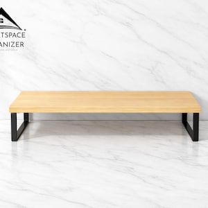 May include: A rectangular wooden desk riser with a light brown surface and black metal legs. The product is branded with the text "SMARTSPACE ORGANIZER For Home and Office". The riser is designed to elevate a monitor or other items.