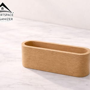 Puede incluir: Un organizador de escritorio de madera de color marrón claro, de forma ovalada. El organizador tiene un acabado liso y está diseñado para guardar objetos pequeños. El logotipo "SMARTSPACE ORGANIZER" es visible en la esquina superior izquierda.