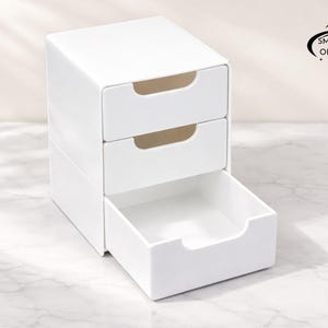 Può includere: Un organizer bianco a due cassetti, con un terzo cassetto parzialmente aperto. L'organizer ha un design minimalista con bordi curvi e maniglie incassate. Il logo Smartspace Organizer è visibile.
