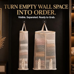 Op de afbeelding: Twee beige hangende opbergorganizers van gaas met handvatten aan de bovenkant en openingen aan de onderkant, gevuld met gevouwen textiel. De tekst luidt: TURN EMPTY WALL SPACE INTO ORDER. Visible. Separated. Ready to Grab.