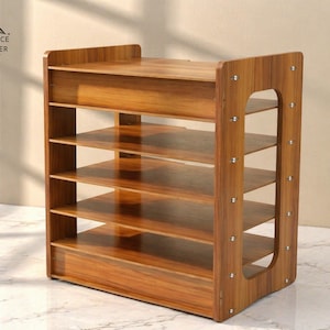 Pode incluir: Um sapateira de madeira com várias prateleiras. A sapateira é feita de madeira castanha clara com um grão de madeira visível. As laterais têm um design curvo com detalhes metálicos decorativos. O texto "SMARTSPACE ORGANIZER" está no canto superior esquerdo.