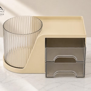 Op de afbeelding: Een beige bureau-organizer met een doorzichtige, geribbelde cilindrische beker, een kleine lade en twee grijze lades. De organizer heeft de tekst "SMARTSPACE ORGANIZER" in de linkerbovenhoek.
