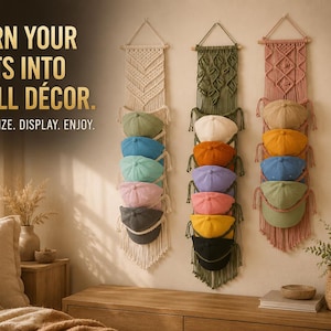 Op de afbeelding: Drie macramé wandhangers in crème, olijfgroen en oudroze, elk voorzien van meerdere vakken voor het opbergen van diverse gekleurde baseballpetten. De tekst luidt: TURN YOUR HATS INTO WALL DÉCOR. ORGANIZE. DISPLAY. ENJOY. Verticaal opgehangen.