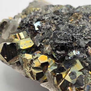 Puede incluir: Primer plano de un espécimen mineral de pirita y cuarzo. Los cristales de pirita tienen un color dorado metálico y formas geométricas. El cuarzo es translúcido y blanco, con una superficie rugosa y texturizada. La apariencia general es de una formación mineral natural en bruto.