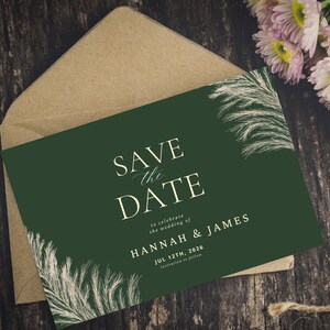 May include: A dark green wedding save-the-date card with the text "SAVE the DATE" in elegant white script. The card includes the names "HANNAH & JAMES" and the date "JUL 12TH, 2026". The card is inside a brown envelope.