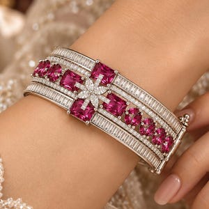 Può includere: Un ampio bracciale rigido color argento con file di pietre trasparenti taglio baguette e una fascia centrale orizzontale di gemme rosa vivace quadrate e rotonde. Un piccolo motivo floreale di pietre trasparenti si trova al centro.