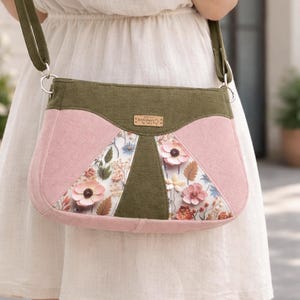 以下が含まれることがあります： ピンクとオリーブグリーンのフローラルデザインのクロスボディバッグ。 フラップ開閉と調節可能なストラップが付いています。 フローラルパターンにはピンクの花と緑の葉が含まれています。 バッグは布製です。