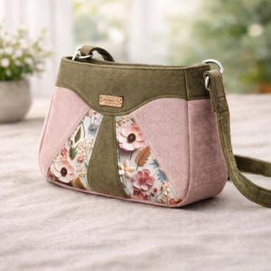 May include: A pink and olive green crossbody bag with a floral design on the front. The bag has a corduroy texture and an adjustable strap. A small, rectangular tag with the script text "sewcheese" is attached to the bag.