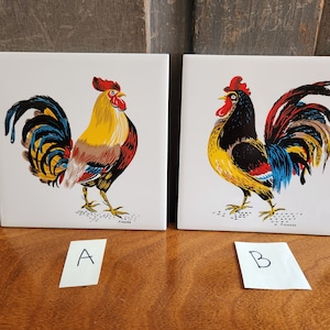 May include: Two vintage ceramic tiles featuring colorful rooster illustrations. The rooster on the left tile is yellow, red, and blue. The rooster on the right tile is black, yellow, red, and blue.