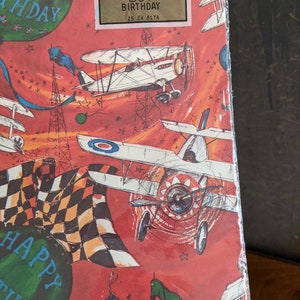 Pu&ograve; includere: Carta da regalo rossa e bianca con una bandiera a scacchi, aerei e stelle. La carta dice "Happy Birthday" e "Hallmark Boy Birthday 25 EV 5174". Dice anche "2 sheets 20 1/4" x 28 1/2" 25c".