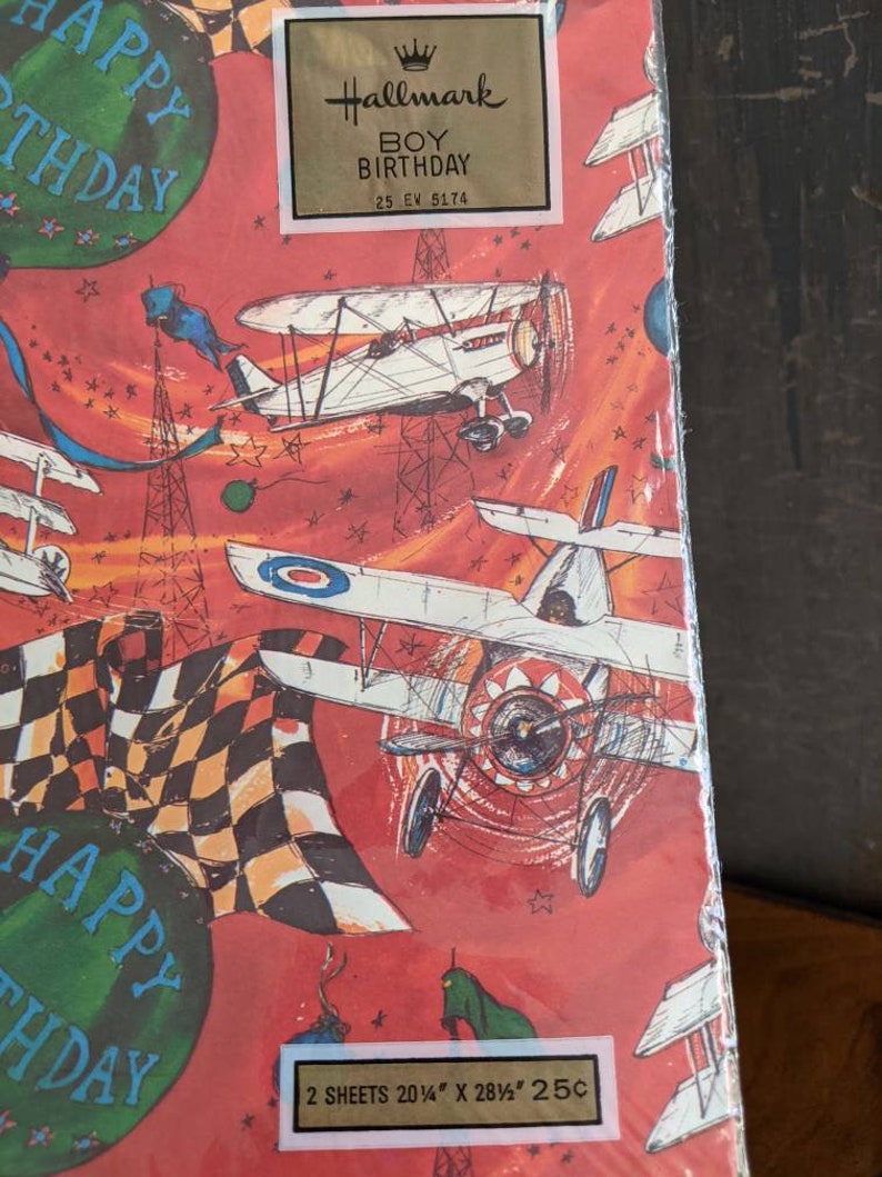 Pu&ograve; includere: Carta da regalo rossa e bianca con una bandiera a scacchi, aerei e stelle. La carta dice "Happy Birthday" e "Hallmark Boy Birthday 25 EV 5174". Dice anche "2 sheets 20 1/4" x 28 1/2" 25c".