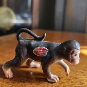May include: A brown ceramic monkey figurine with a red and white label that reads "Bone China Shiken Japan".