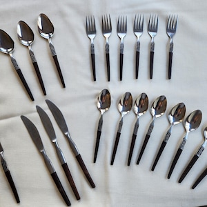 May include: A collection of stainless steel flatware with dark brown handles. The set includes spoons, forks, and knives, arranged on a white surface. The handles have a decorative silver band near the top.