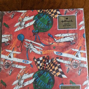 Pu&ograve; includere: Carta da regalo vintage Hallmark con sfondo rosso e un motivo ripetuto di aerei, palloncini e bandiere a scacchi. La carta dice "Happy Birthday" in un palloncino verde e "Boy Birthday" in un rettangolo dorato. La carta &egrave; composta da 2 fogli, 20 1/4" x 28 1/2" e costa 25 centesimi.