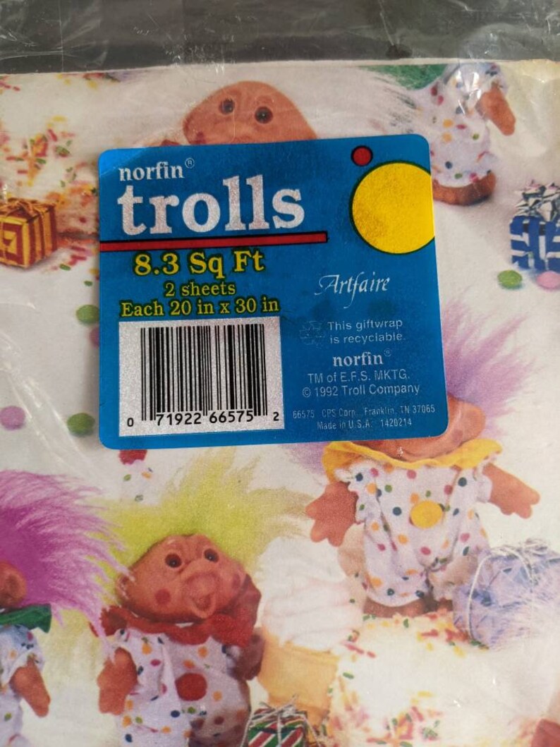 Pu&ograve; includere: Un pacchetto di carta da regalo blu e gialla con un'illustrazione colorata di troll. Il pacchetto dice "norfin trolls 8.3 Sq Ft 2 sheets Each 20 in x 30 in".