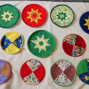 May include: Ten colorful quilted pot holders with various patterns, including stars, polka dots, and floral designs. The pot holders are circular and have a green, red, yellow, blue, and white color scheme.
