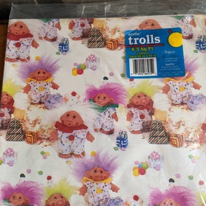 Pu&ograve; includere: Carta da regalo con un motivo ripetuto di troll colorati con cappelli festivi e coriandoli. La carta &egrave; bianca con uno sfondo blu chiaro. Il testo sull'etichetta dice "norfin trolls 8.3 Sq Ft 2 sheets Each 20 in x 30 in Artfaire This giftwrap is recyclable norfin Total E.P.S. 1.8KG &copy; 1992 Troll Company 71922 66575 2"