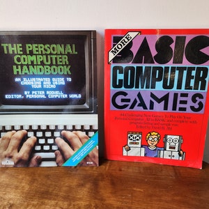 May include: Two vintage computer books with red and blue covers. The book on the left is titled "The Personal Computer Handbook" and the book on the right is titled "More Basic Computer Games".