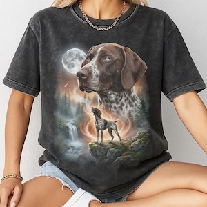 May include: Dark gray t-shirt featuring a detailed illustration of a German Shorthaired Pointer with a full moon and waterfall backdrop. The design includes a large dog portrait and a smaller dog standing on a cliff.