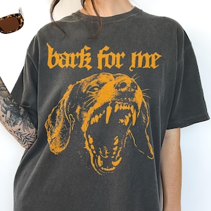 Black vintage t-shirt featuring a high-contrast orange graphic of a snarling Dachshund dog showing teeth, with the text bark for me in gothic font above it, grunge streetwear style.