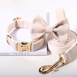 May include: A beige dog collar, bow tie, and leash set with gold-colored hardware. The collar buckle is engraved with a name and phone number. The bow tie and leash have a herringbone pattern.
