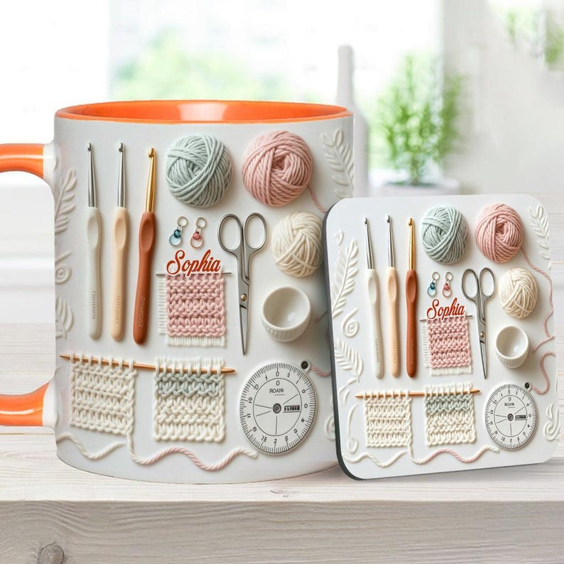 May include: White ceramic mug and coaster set featuring a crochet theme. The mug has an orange interior and handle, with embossed crochet hooks, yarn balls, scissors, and a gauge. The coaster mirrors the design, including the name "Sophia".