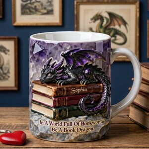May include: A ceramic mug with a dragon design. The mug features a black and purple dragon resting on a stack of books. The mug has the text "In A World Full Of Bookworms Be A Book Dragon."