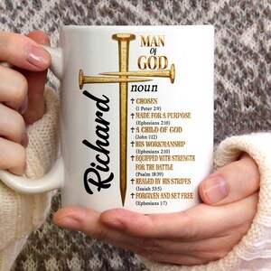 May include: White ceramic mug with the name "Richard" in black script. The mug features a gold cross design with the words "MAN OF GOD" and various religious phrases in gold lettering. The mug is held by a person.