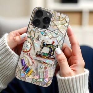 May include: A clear phone case with a mosaic design and sewing-themed illustrations. The case features a sewing machine, scissors, spools of thread, and the name "Isabella". The design incorporates iridescent and colourful elements.