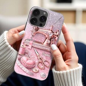 May include: A pink and silver phone case with a rose gold sewing machine, scissors, and a heart-shaped pin cushion. The case includes the name "Sophia" and a measuring tape. The design has a glittery background and a clear border.