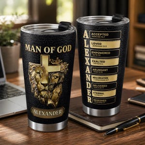 May include: Two black stainless steel tumblers with lids. One features a gold lion and praying figure behind a cross with the text MAN OF GOD and ALEXANDER. The other displays the name ALEXANDER vertically with gold labels listing biblical verses.