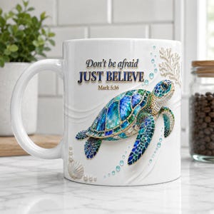 Puede incluir: Una taza de cerámica blanca con una tortuga marina colorida con caparazón y piel de patrones azules y verdes. El texto "Don't be afraid JUST BELIEVE Mark 5:36" está impreso en negro y azul. El diseño incluye detalles de coral blanco y perlas.