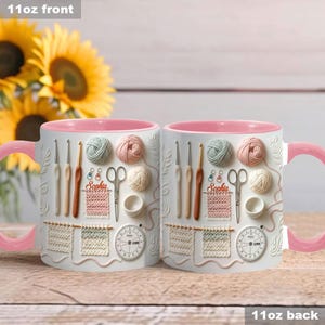 May include: Two white ceramic mugs with pink handles and interiors. The mugs feature a 3D design of knitting and crochet tools, yarn balls, and a clock. The name "Sophia" is printed on the mugs.